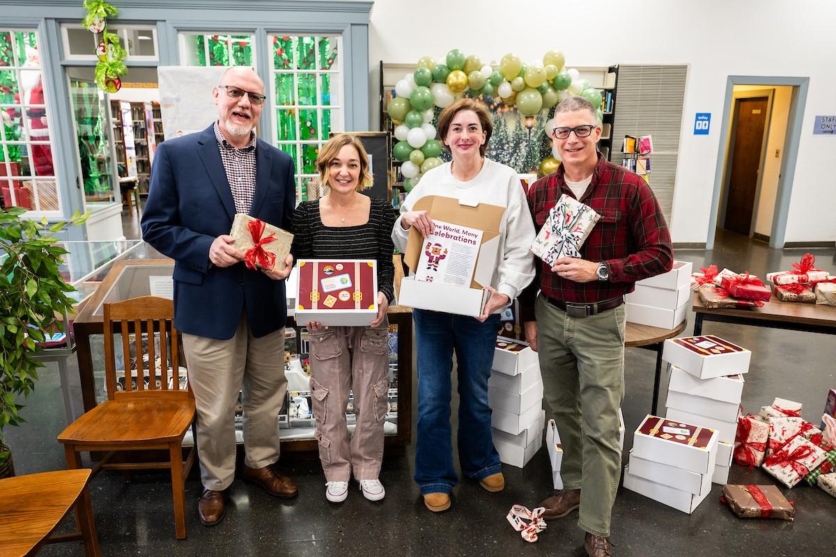 Four people standing in front of a table full of Bulldog Explorers box. Two are holding wrapped gifts and two are holding Bulldog Explorer boxes.